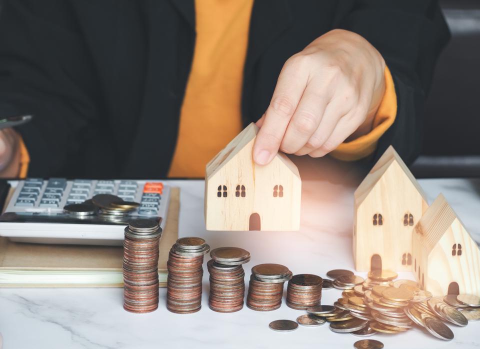 Female's hand put wood house model with stack coin staircase on desk.