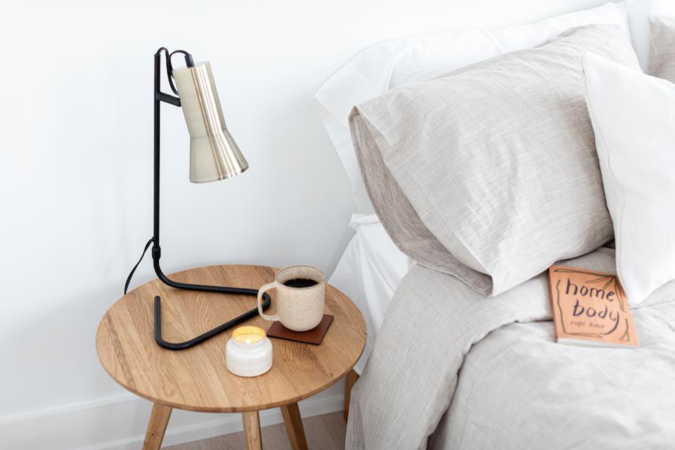 A bed with linen bedding next to a wood table with coffee and a lamp