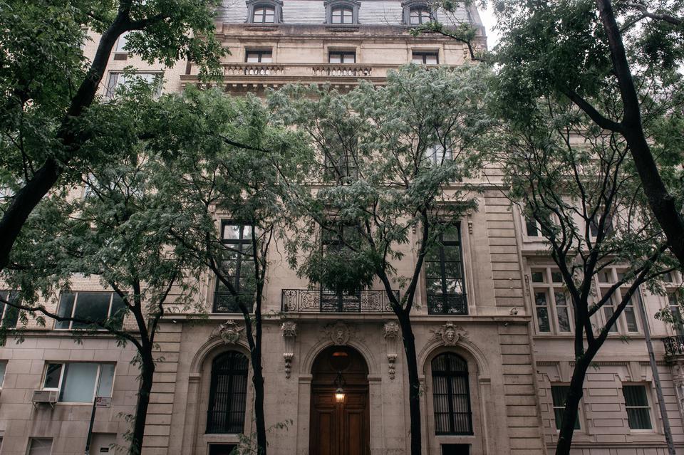 Neoclassical mansion with tall leafy trees.