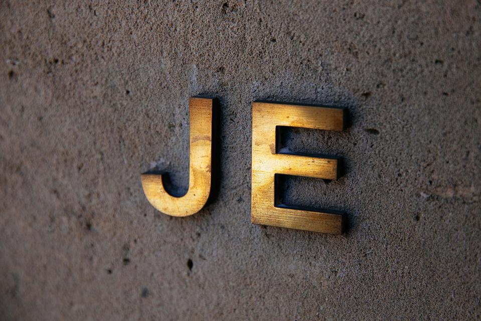 Brass initials J.E. on white concrete.
