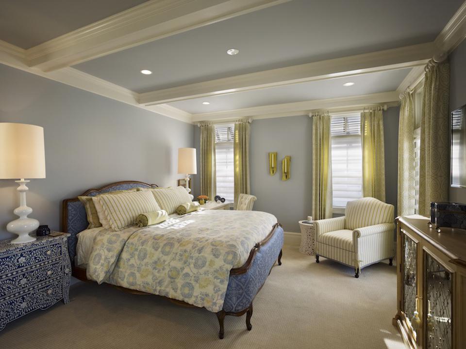 A blue bedroom with a dresser on one side of bed.