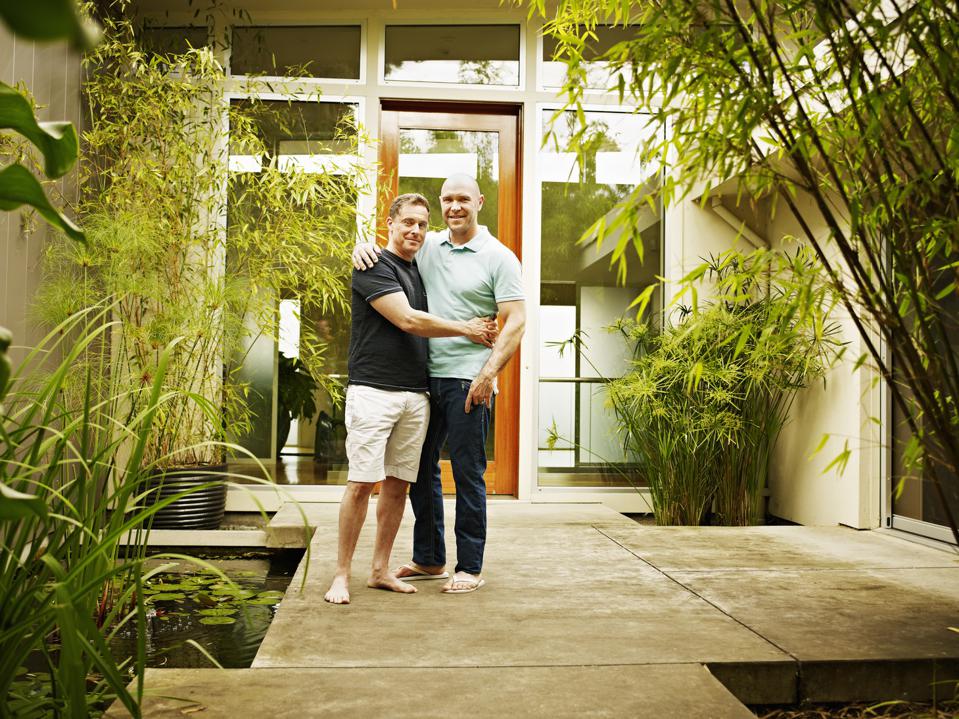 Smiling gay couple in front of contemporary home